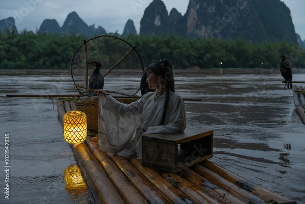Obraz Hanfu girl holding an illuminated lantern on a bamboo raft with Cormorant birds at night