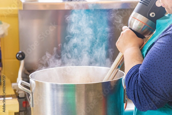 Fototapeta Chef is using an immersion blender in a large pot while preparing food in a professional kitchen. Selective focus