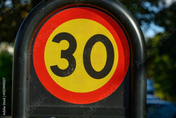 Obraz A circular speed limit sign displays a 30 kph limit, prominently situated in a residential neighborhood under clear, natural lighting
