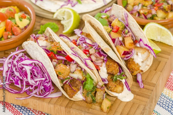 Fototapeta Baja Fish Tacos - tacos o miękkiej skorupce wypełnione przyprawioną smażoną białą rybą podawane z czerwoną kapustą, salsą ananasową, chrupiącym guacamole i kremowym sosem Baja.