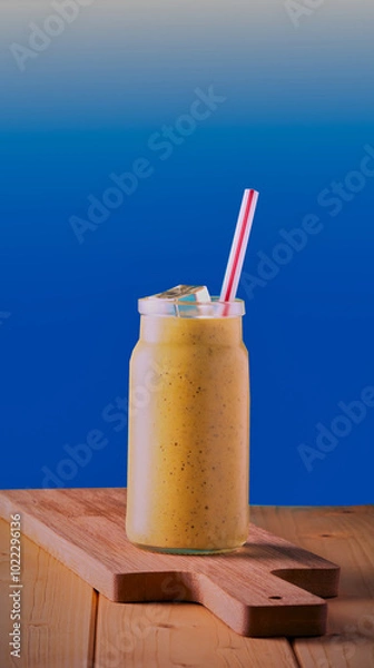 Fototapeta Healthy smoothie in a jar with a straw and ice on a blue gradient background.