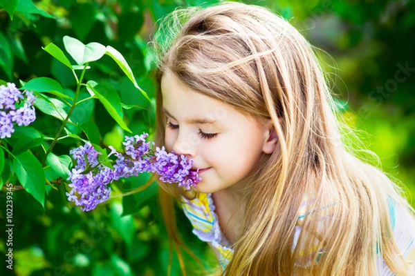 Obraz Beautiful blond little girl with long hair smelling flower on sunny day in summer park