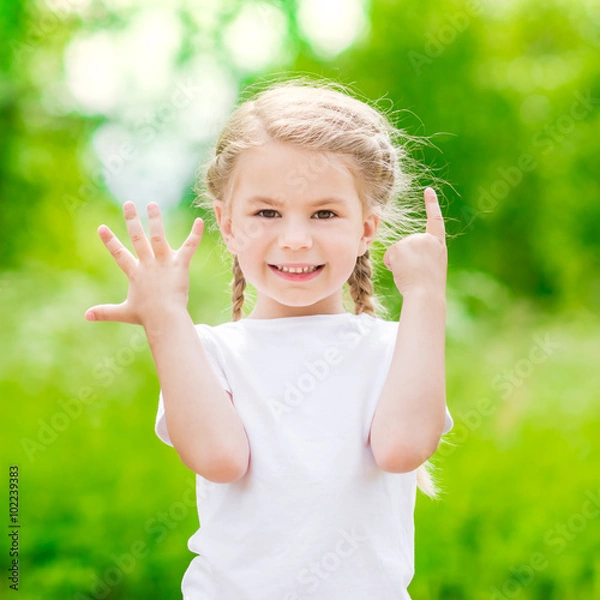 Obraz Beautiful blond little girl with two braids  showing six fingers (her age) and smiling on sunny day in summer park