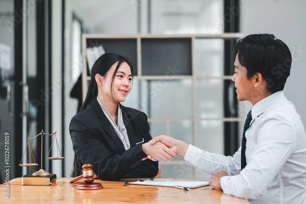 Obraz Two business professionals shaking hands across a table in a modern office, symbolizing agreement and partnership.