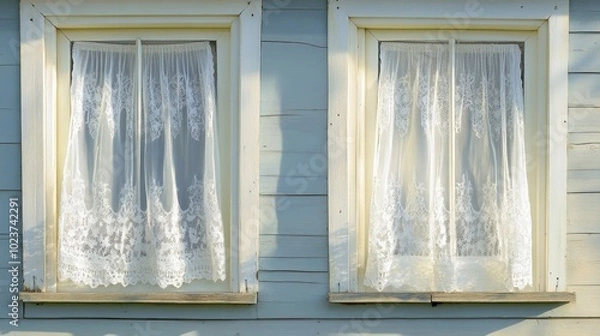 Fototapeta A pair of windows with delicate lace curtains gently blowing in the breeze on a summer day.