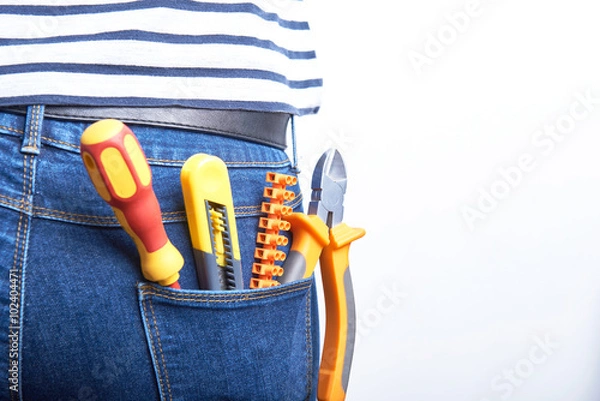 Fototapeta Tools for electrician in back pocket of blue jeans worn by a woman. Screwdriver, sharp knife, cutters and connectors.