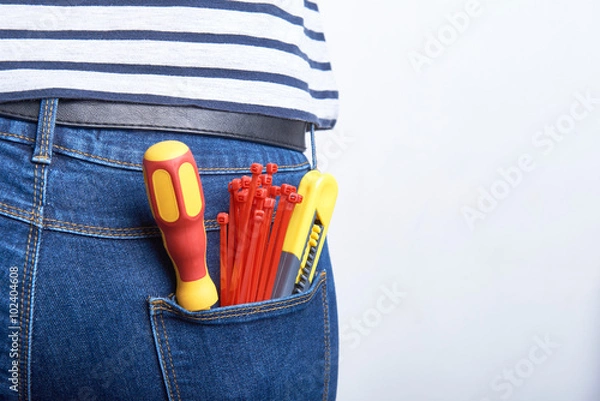 Fototapeta Tools for electrician in back pocket of blue jeans worn by a woman. Screwdriver, sharp knife and zip ties.