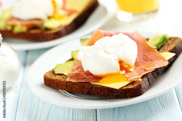 Obraz Poached eggs with avocado and bacon on toasts on blue wooden tab