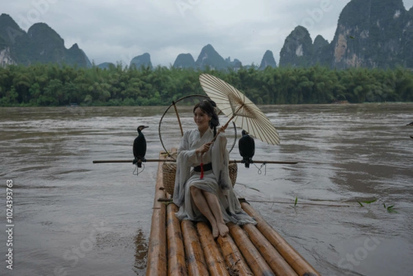 Obraz Hanfu girl with umbrella on bamboo raft in Xingping posing with cormorants