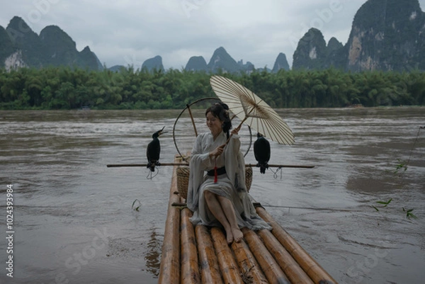 Obraz Hanfu girl with umbrella on bamboo raft in Xingping posing with cormorants