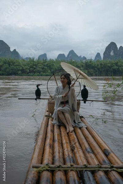 Obraz Hanfu girl with umbrella on bamboo raft in Xingping posing with cormorants