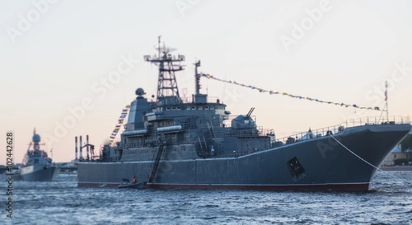 Fototapeta Grey modern battleship warship sailing in still water against summer sky with one more warship in the background