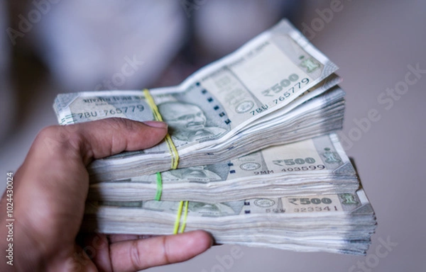 Fototapeta a hand holds multiple bundles of ₹500 Indian rupee notes, neatly stacked and tied with rubber bands, showcasing financial abundance and control over wealth. 