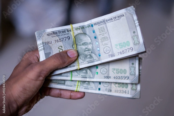 Fototapeta a hand holds multiple bundles of ₹500 Indian rupee notes, neatly stacked and tied with rubber bands, showcasing financial abundance and control over wealth. 