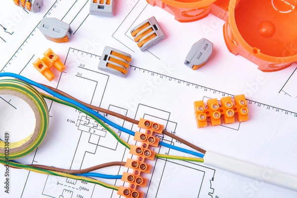 Fototapeta Electrical connectors with wires, junction box and different materials used for jobs in electricity. Many tools 

lying on diagrams. Concept of electrical works.

