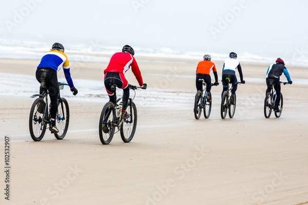 Fototapeta pięć nierozpoznawalnych osób jeździ na rowerach górskich po plaży podczas zawodów.