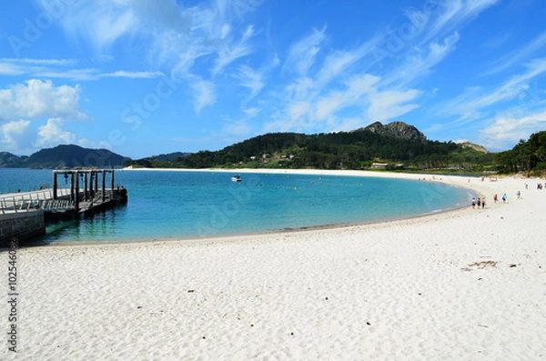 Fototapeta General view of a beautiful semicircular beach (Playa de Rodas) in the Cies Islands. It can be seen the pier and unidentified people.

