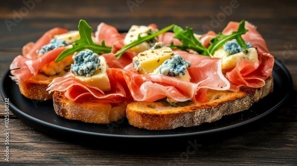 Obraz Close-up of three crostini topped with prosciutto, blue cheese, and arugula on a black plate.