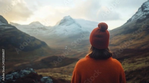 Obraz A person in a bright orange sweater and red hat admires stunning mountain scenery at sunset. Nature captivates with its beauty.