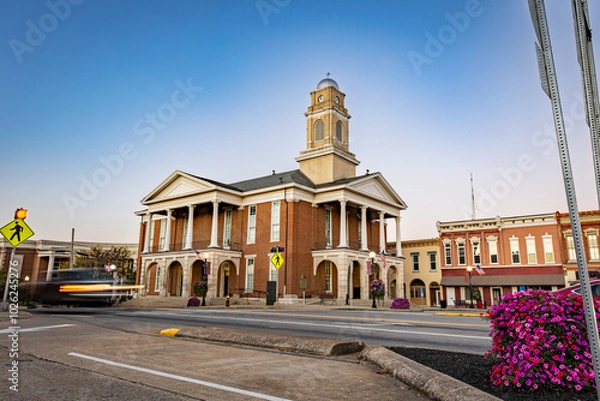 Fototapeta Morning traffic headlights illuminate the downtown square in Lancaster, Kentucky, with the historic courthouse as a backdrop in this small American town.