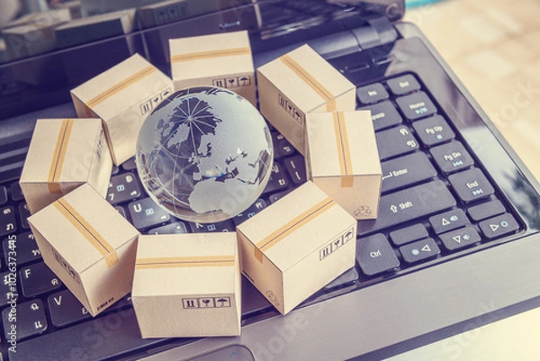 Fototapeta International freight or shipping service for online shopping or ecommerce concept : Paper boxes or carton put in circle around a clear crystal globe with world map on a computer notebook keyboard.