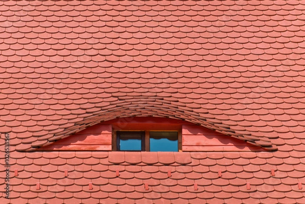 Fototapeta A close-up view of a renovated traditional red clay roof with a curved dormer window in Sibiu, Romania. The window features a rectangular shape and glass panes.
