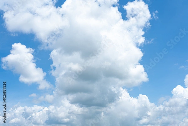 Fototapeta Fluffy cumulus clouds drift across a bright blue sky, painting a beautiful summer day