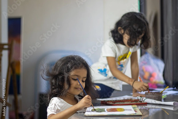 Fototapeta Two sisters are doing art work with water color on paper at home.