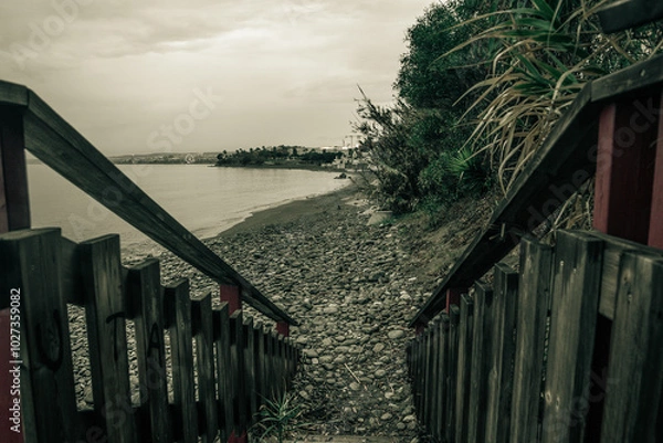 Fototapeta Escalera de madera que lleva hacia la playa un día nublado