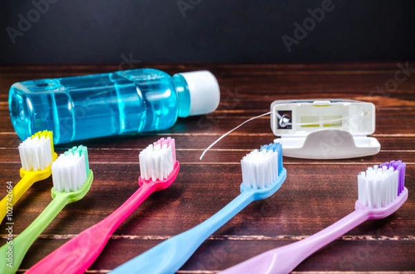 Obraz Set of colorful toothbrush with mouthwash and dental floss on wooden board