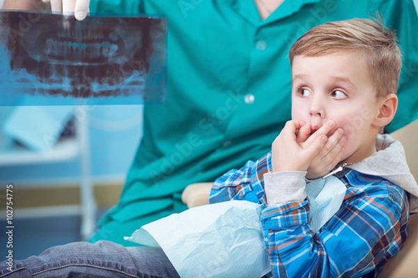 Fototapeta Dental inspection is being given to little boy surrounded by dentist and his assistant, showed him a photo of the teeth