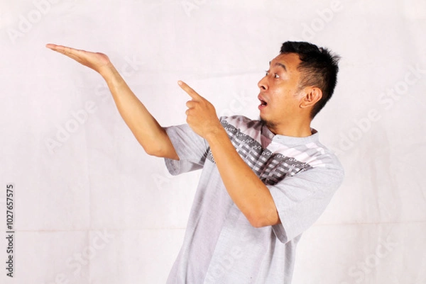 Fototapeta Asian adult man smiling happily after getting a new idea with his pose opening his arms and showing his idea