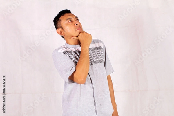 Fototapeta Mature Asian man thinking with pensive expression wearing blue shirt with hand on chin
