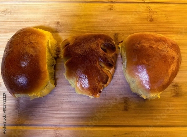 Obraz Three golden-brown Ukrainian pyrizhky (filled buns) rest on a wooden cutting board, each with a shiny, perfectly baked crust. These traditional pastries are a beloved part of Ukrainian cuisine.