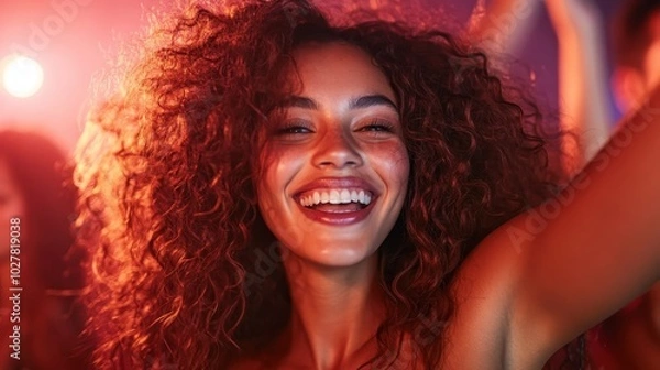 Fototapeta A cheerful woman with curly hair laughs and enjoys herself surrounded by a lively crowd in a vibrant and festive club ambiance with glowing lights.