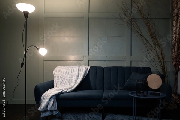 Fototapeta A cozy living room corner with a blue sofa, warm lighting, and decorative elements in an inviting space during the evening