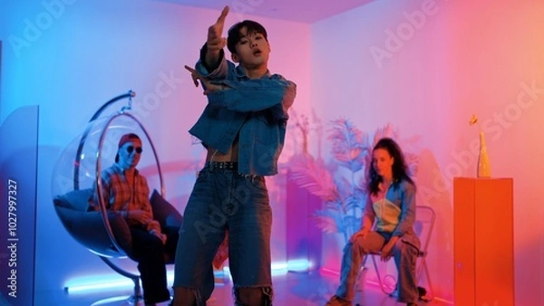 Fototapeta Skilled asian dancer moving to modern music while multicultural friend sitting at chair. Professional performer dancing show energetic foot step while hipster team cheering and supporting. Regalement.