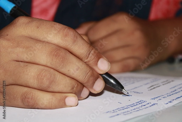 Fototapeta Close-Up of a woman is writing on a piece of paper with a pen with Blurred Background