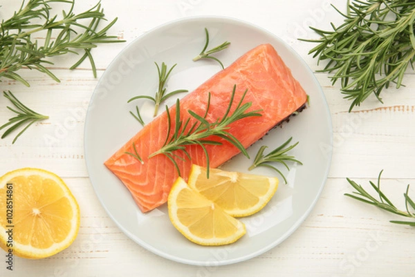 Fototapeta Red fish. Raw salmon fillet with rosemary and lemon on grey plate on white background.