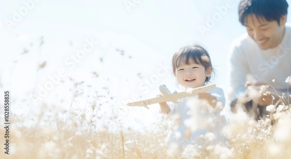 Obraz 明るい陽光の中で飛行機の模型を持って遊ぶ幼児と父親