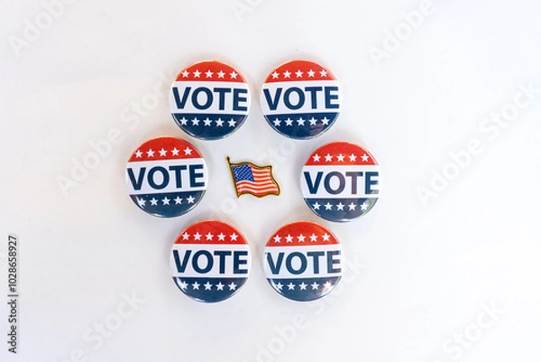 Fototapeta Vote buttons and American flag pin on white background. A collection of red, white, and blue "Vote" buttons arranged in a circular pattern around a small American flag pin symbolizing patriotic voting