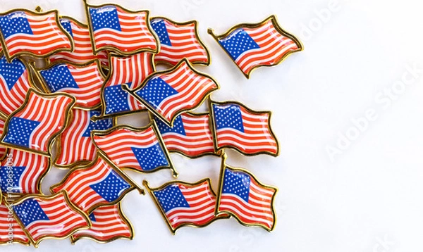 Fototapeta Collection of American flag pins on white background. Small American flag pins scattered on a white surface. The pins feature the iconic red, white, and blue design with gold edges,patriotism 
