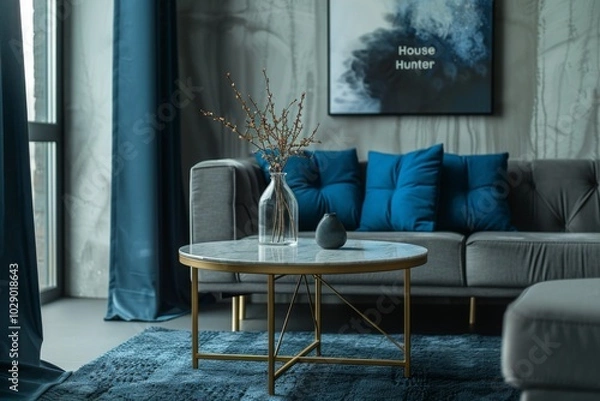 Fototapeta Modern and contemporary side tables with grey stone top on brass legs, near a gray sofa with blue pillows, in a minimalist living room.