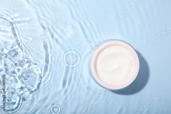 Obraz Cosmetic product. Jar with cream in water on light blue background, top view. Space for text