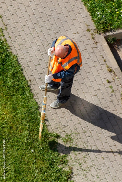Obraz A man in an orange vest is sweeping the sidewalk