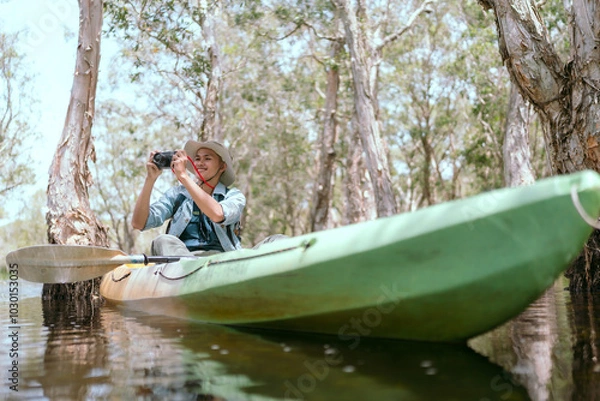 Fototapeta A young Asian man travels alone in the jungle, paddling a boat and taking photos alone.