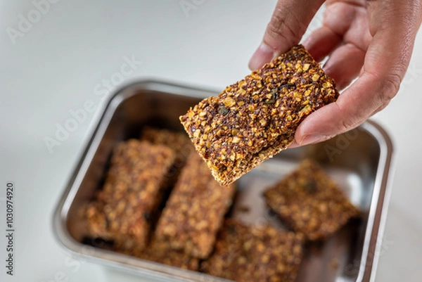 Fototapeta holding muesli bar in the hand with more in the container in background