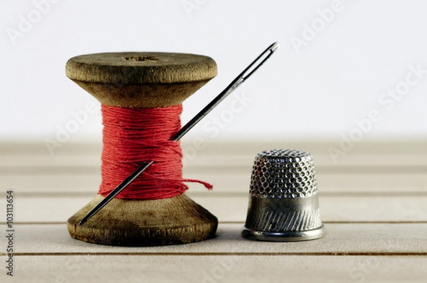 Fototapeta Vintage spool of thread with needle closeup. Tailor's work table, textile or fine cloth making.
