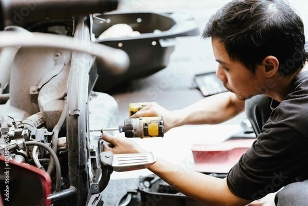 Obraz Motorcycle mechanic uses electric screwdriver ,power tool to repair motorcycle in garage,Checking and removing damaged motorcycle parts  ,Maintenance and repair concept