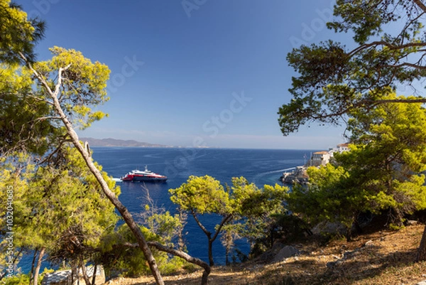 Obraz The Hydra boat port showcases a vibrant catamaran floating in sparkling waters, surrounded by greenery and distant mountains beneath a bright sky.